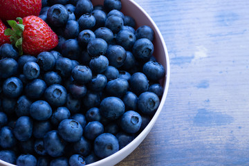 Bowl of blueberries and strawberries in a pink bowl on a wooden surface.