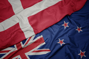 waving colorful flag of new zealand and national flag of denmark.