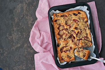 Sponge cake with plum and shtrezel in a black baking dish on a dark concrete background. Harvest plums. Recipes with plums. German food. Top view, copy space.