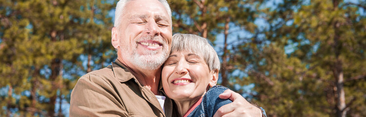 panoramic view of happy senior couple embracing with smile and closed eyes