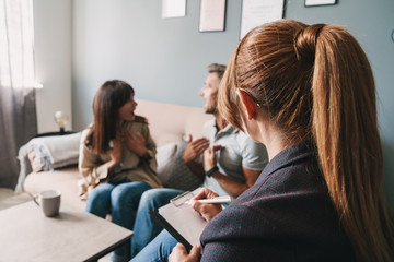 Photo of angry nervous couple having conversation with psychologist on therapy session in room