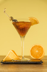 Red alcoholic cocktail in transparent glass with citrus and olives on a wooden table