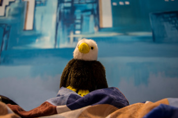 Fluffy eagle toy proudly sitting on sheets with a city background