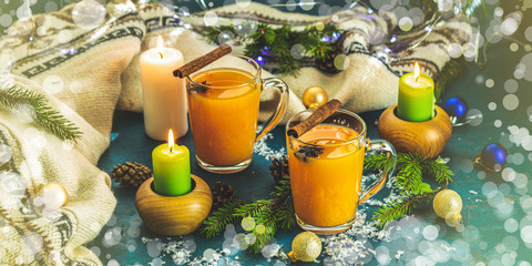 Christmas and New Year banner composition with two cup of hot spicy tea, candles and holiday decor, bokeh, dark background.