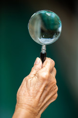 Senior woman's right hand holding old broken magnifying glass on bokeh blue swimming pool background, Close up shot, Selective focus