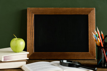 Teacher's Day. Blank slate blackboard, textbooks, apple and magnifier glass on the school desk