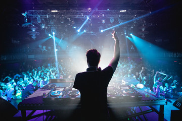 Silhouette of DJ in nightclub with hands up, shot from behind - obrazy, fototapety, plakaty