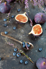 Blueberries, figs, halves of figs and heather sprigs on a dark textured concrete surface. Lovely autumn still life. Seasonal fruits and berries for a healthy life. Top view at an angle, close up.