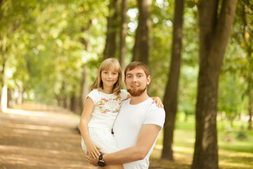 Portrait of lovely smiling daughter in her father's arms walking at green park outside. Happy family people concept