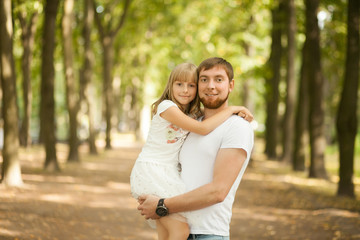 Fototapeta premium Portrait of lovely smiling daughter in her father's arms walking at green park outside. Happy family people concept