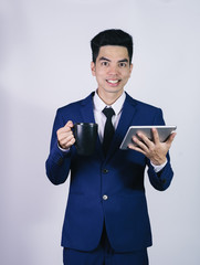 Portrait handsome young asian man wearing a blue suit holding smart phone or tablet smile and happy isolated on gray background in studio. Asian man people. business success concept.