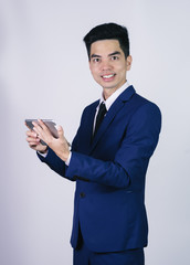 Portrait handsome young asian man wearing a blue suit holding smart phone or tablet smile and happy isolated on gray background in studio. Asian man people. business success concept.