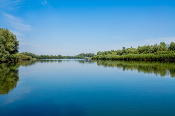 Fototapeta na wymiar Blue beautiful sky against the background of the river. Clouds are displayed in calm water. On the horizon, the green bank of the Dniester, place for fishing