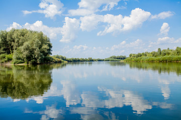 Obraz na płótnie Canvas Blue beautiful sky against the background of the river. Clouds are displayed in calm water. On the horizon, the green bank of the Dniester, place for fishing