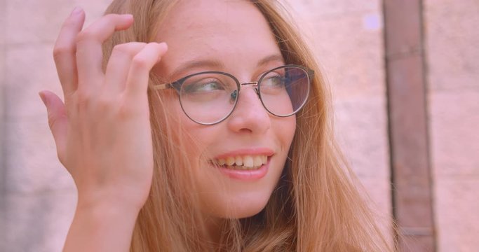Closeup portrait of young attractive caucasian female with long hair in glasses looking at camera smiling happily with wind blowing outdoors