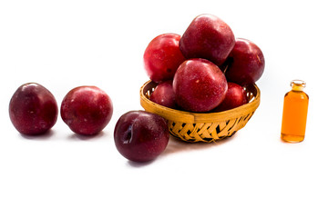Raw organic red ripe plums in a brown-colored basket along with its extracted essential oil in a small transparent bottle isolated on white.Easy to cut and remove from the background and to use it.