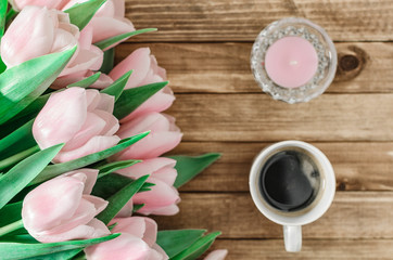 Background with bouquet of pink tulips on brown wooden boards with cup of coffee and candle. Copy space. Top view. Toned image. Horizontal