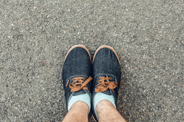 A man stands on an asphalt street, feet in blue boots and socks, close up, top view, background, copy space, advertising