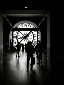 Silhouettes of tourists visiting d'Orsay Museum shot against big external clock