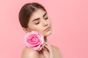 Naklejka premium Close-up portrait of a beautiful young girl with pink rose flower isolated over pink background.
