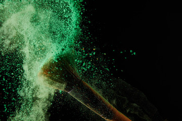 soft cosmetic brush with colorful green powder explosion on black background