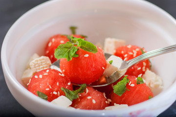Salad of watermelon balls, feta cheese and mint, sprinkled with sesame seeds in a white plate
