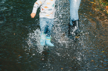 Legs of woman and her little son standing in a puddle of water after rain.