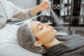 Cometologyst making professional facial hydration to a woman at the beaty salon, close-up view