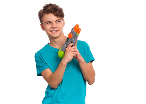 Portrait of happy teen boy playing with plastic water gun, isolated on white background. Beautiful caucasian teenager having fun with children toy. Funny summer games with water.