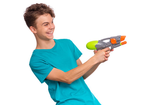Portrait of happy teen boy playing with plastic water gun, isolated on white background. Beautiful caucasian teenager having fun with children toy. Funny summer games with water.