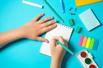 children's hand writes in a notebook in composition with watercolor, pencil, notebooke, ruler, eraser. Isometric concept on blue background. Pop art. School supplies. overhead. back to school concept