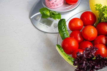 Diet food and measuring tape on a stone background. Cherry tomatoes, lettuce, peppers, cucumbers. Serving Weighing Scales. Concept of diet and healthy lifestyle.