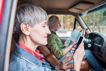 side view of smiling senior woman using smartphone with blank screen while husband looking at map in car