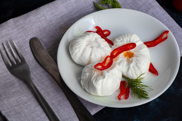 Poached egg - with slices of chili pepper, a sprig of dill, cherry tomatoes. For a healthy breakfast or snack. The plate lies on a gray napkin, there are cutlery. Fork and knife. 