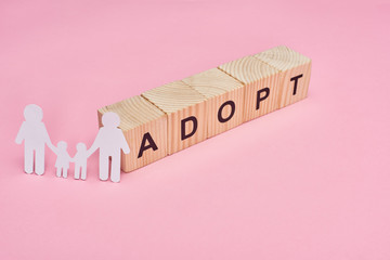 wooden cubes with adopt lettering and paper cut gay family on pink background