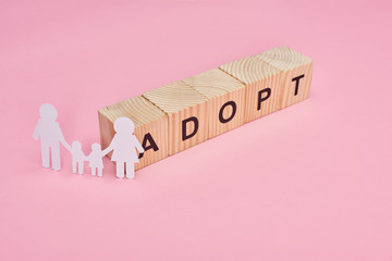 wooden cubes with adopt lettering and paper cut family on pink background