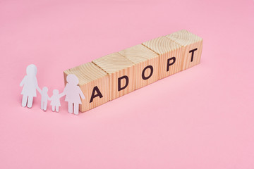 wooden cubes with adopt lettering and paper cut lesbian family on pink background