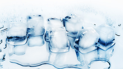 Ice cubes on white glass mirror background with reflection close up top view, transparent frozen...