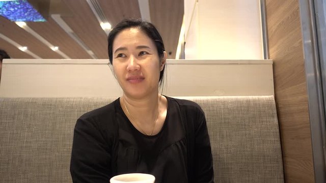 Asian woman wearing a black shirt is sitting at the dining table. She is speaking in a good mood