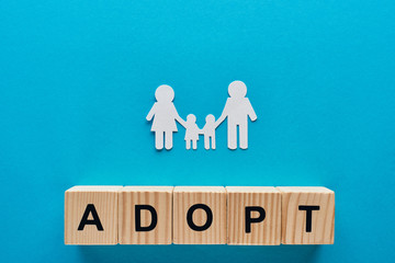 top view of paper cut family holding hands on blue background with adopt lettering on wooden cubes