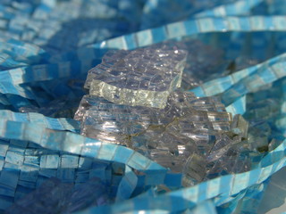 The squares are glass (broken tempered glass) and the squares are blue (plastic).  Contrasts - some hard, sharp, colorless, and other plastic, flexible and colored. shallow focus. close up.