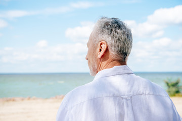 back view of senior man in white shirt at beach in sunny day