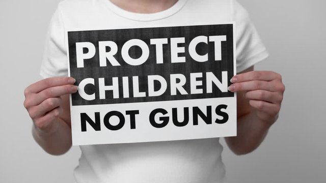 Protect children not guns sign in the hands of unrecognizable young woman in white t-shirt