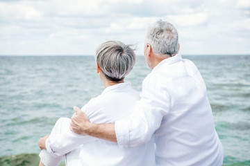Fototapeta na wymiar back view of senior couple in white shirts embracing near river under blue sky