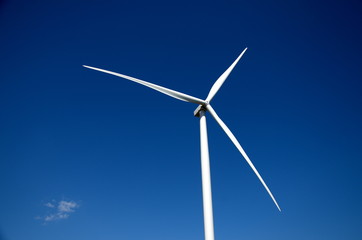 Against a clear blue sky, three blades of a wind farm