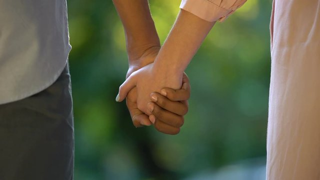 Back view of multiethnic couple holding hands in park, tender romantic feelings