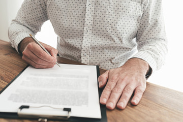 close-up of businessman sitting at wooden desk signing document or contract