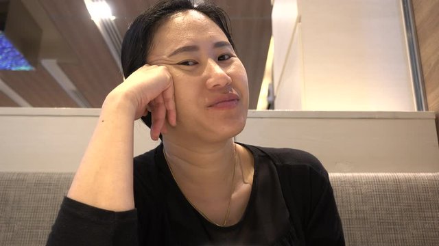 Asian woman wearing a black shirt is sitting at the dining table. She is speaking in a good mood