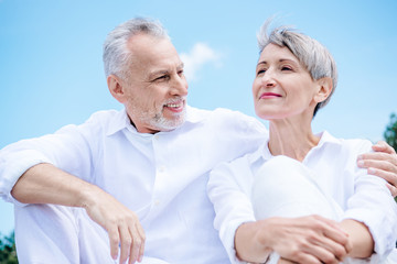happy smiling senior couple in white shirts embracing under blue sky