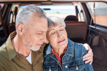 senior couple embracing with closed eyes near car